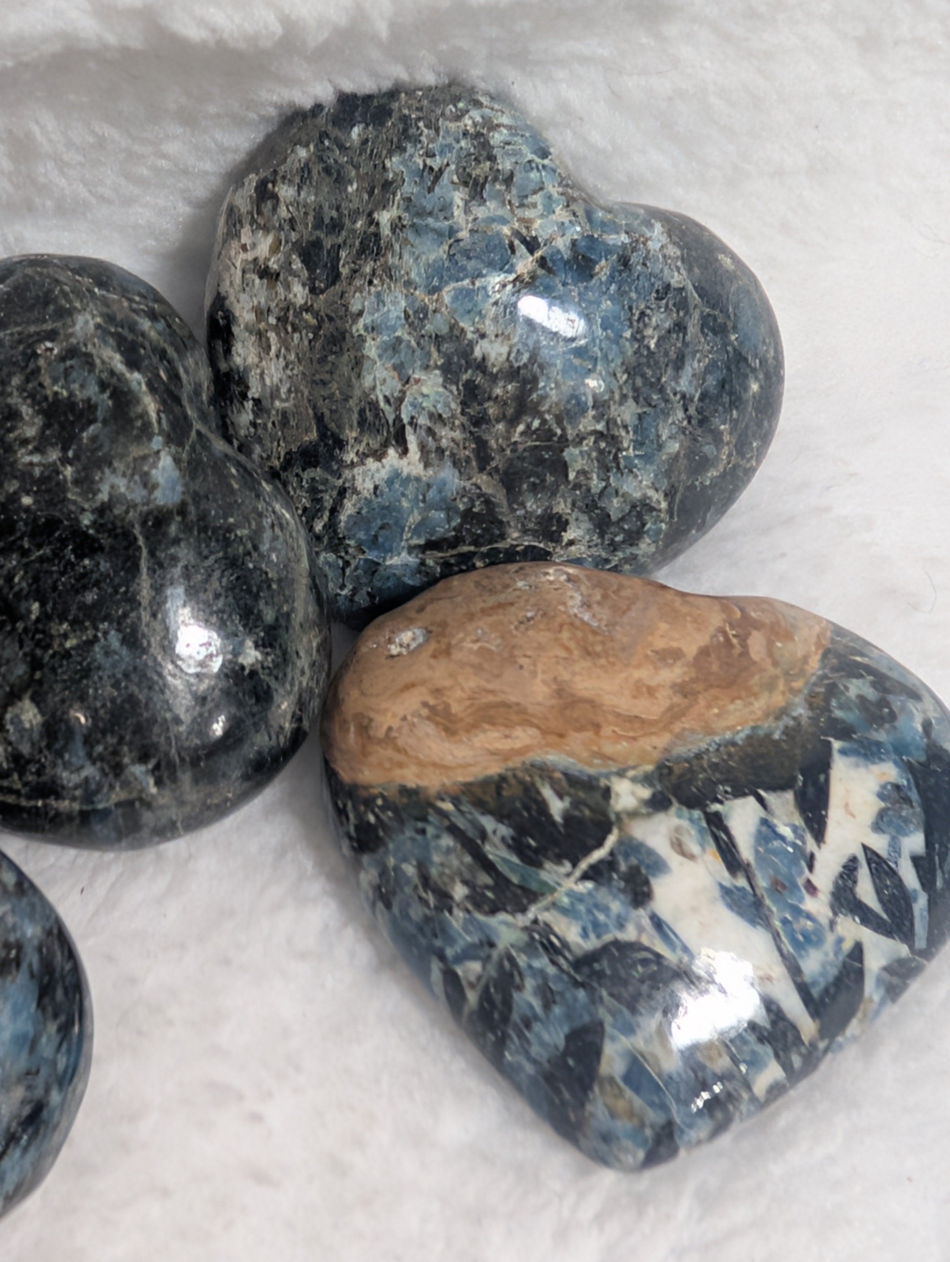 Blue Apatite and Black Tourmaline heart palm stones from Syn's Crystal Co, showing polished stones with vibrant blue and deep black colors.