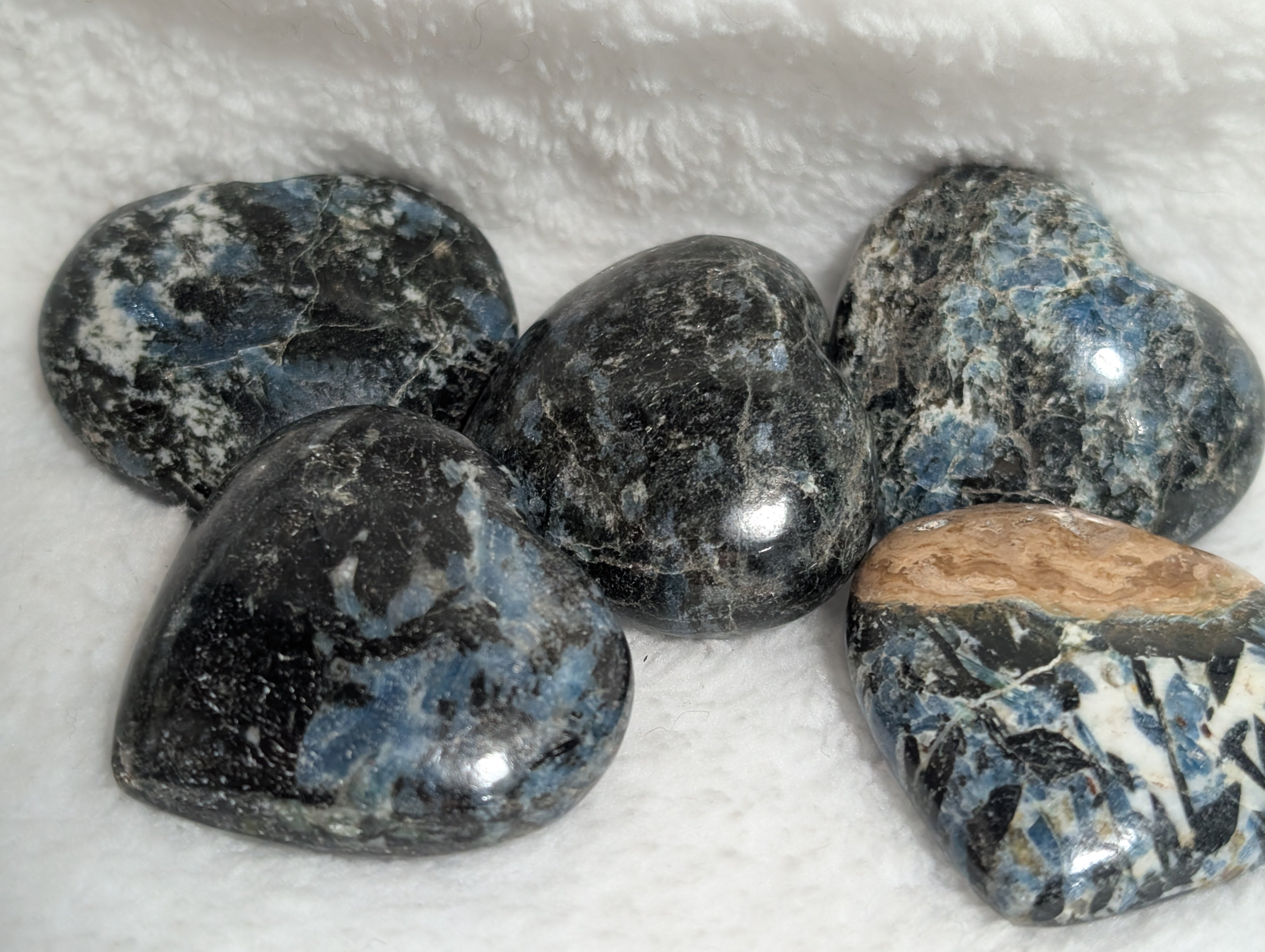 Blue Apatite and Black Tourmaline heart-shaped palm stones from Syn's Crystal Co, showing smooth, polished crystals with vibrant blue and black hues.