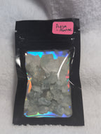 Bag of raw Mookaite crystal chips from Syn's Crystal Co, showing colorful, irregular-shaped natural stone pieces inside a clear bag.