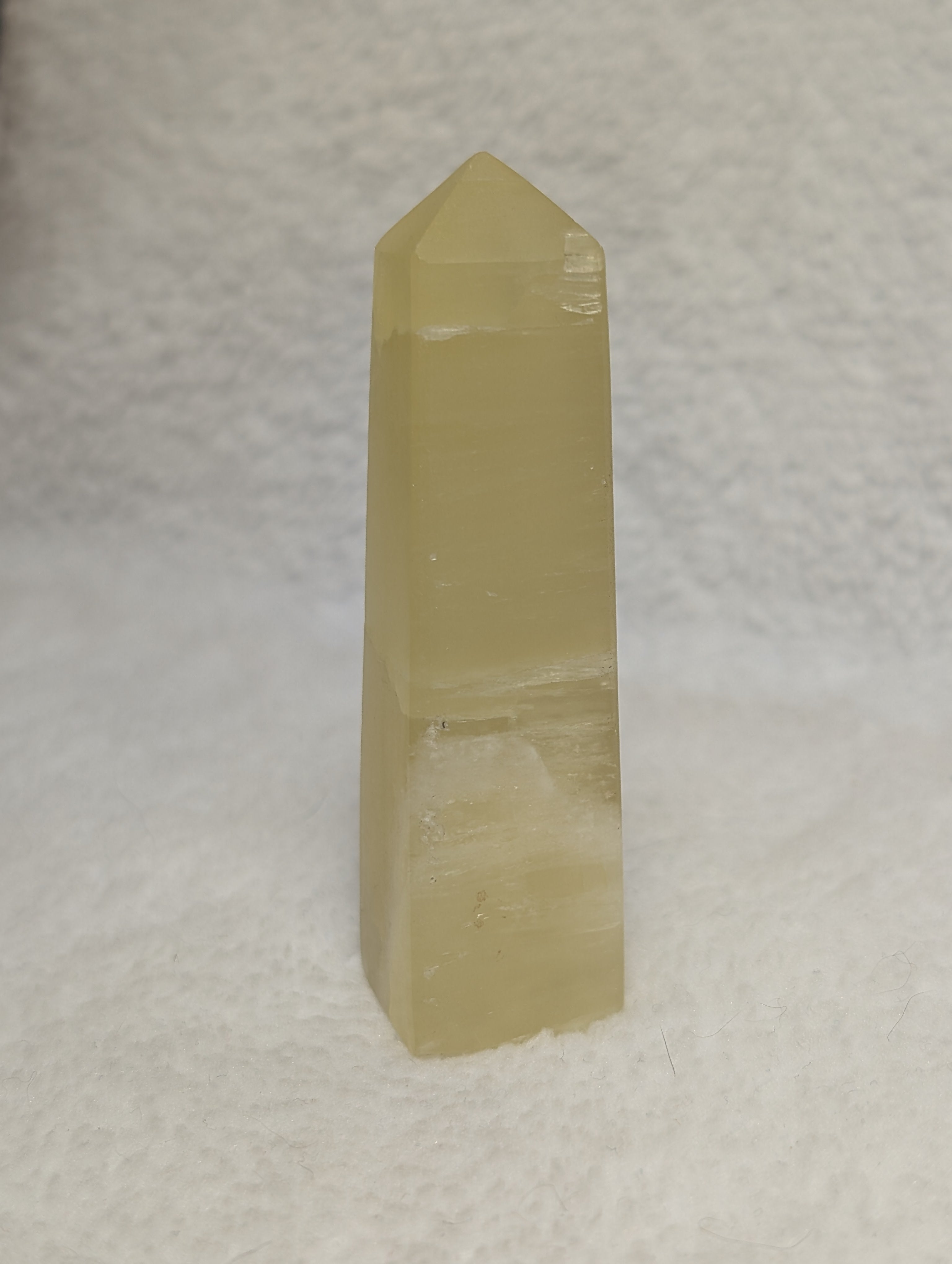 Lemon Calcite Tower by Syn's Crystal Co, a polished yellow crystal with natural striations and a pointed shape.