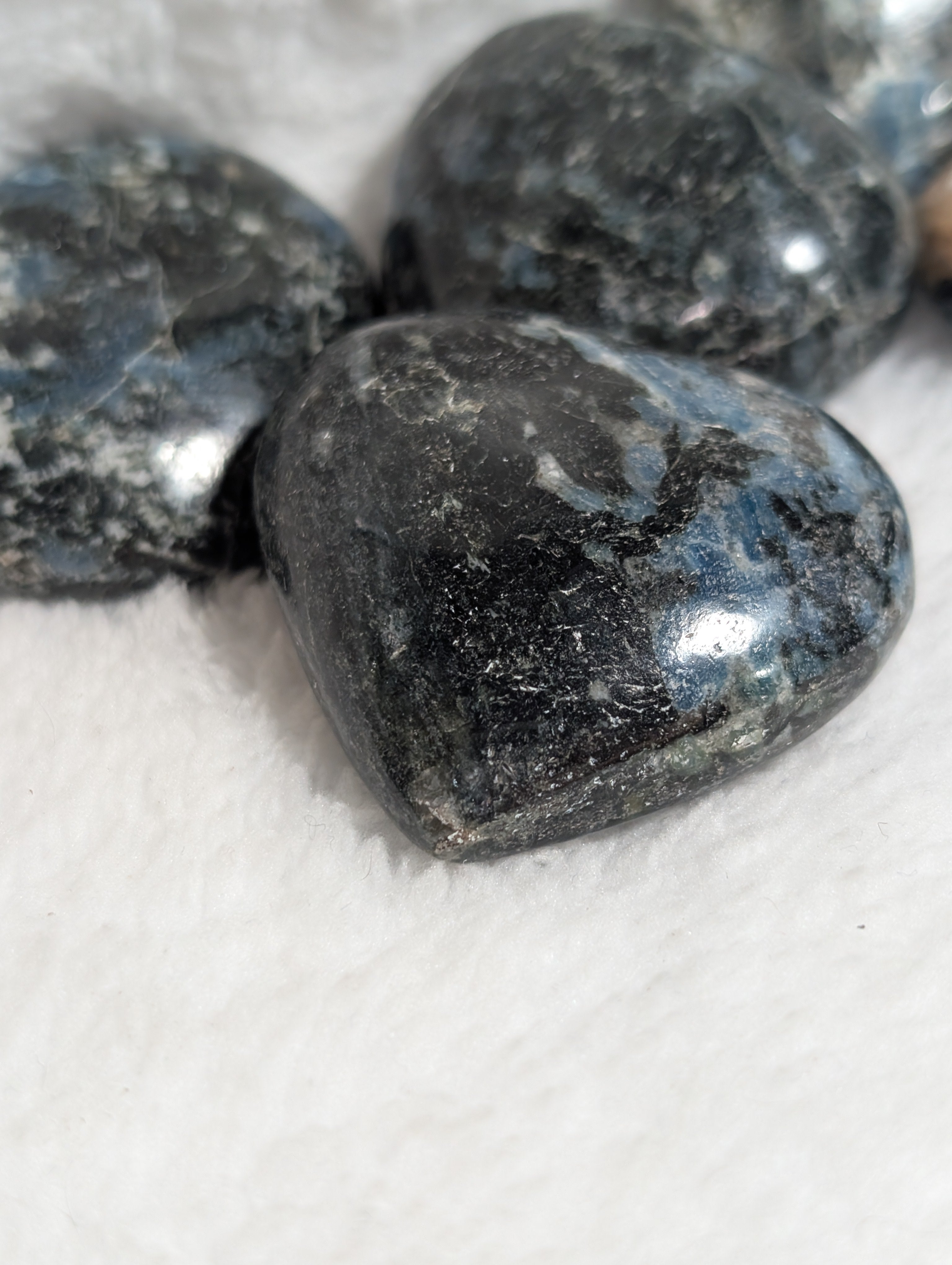 Blue Apatite and Black Tourmaline heart palm stones from Syn's Crystal Co, showing smooth, polished crystals with vibrant blue and dark black colors.