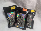 Bag of raw Mookaite crystal chips from Syn's Crystal Co, showing colorful, polished stone fragments in a clear resealable bag.